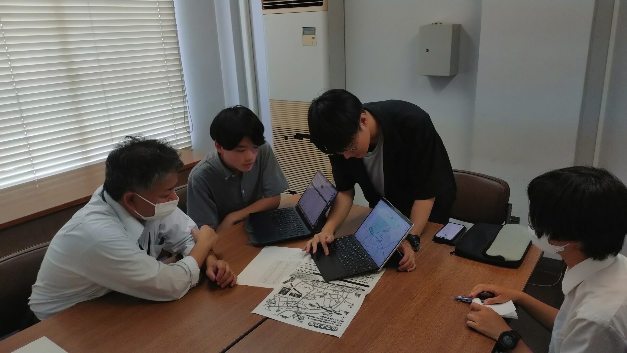 地図やタブレットを使って梨農園の所在地と調査状況を確認する学生
