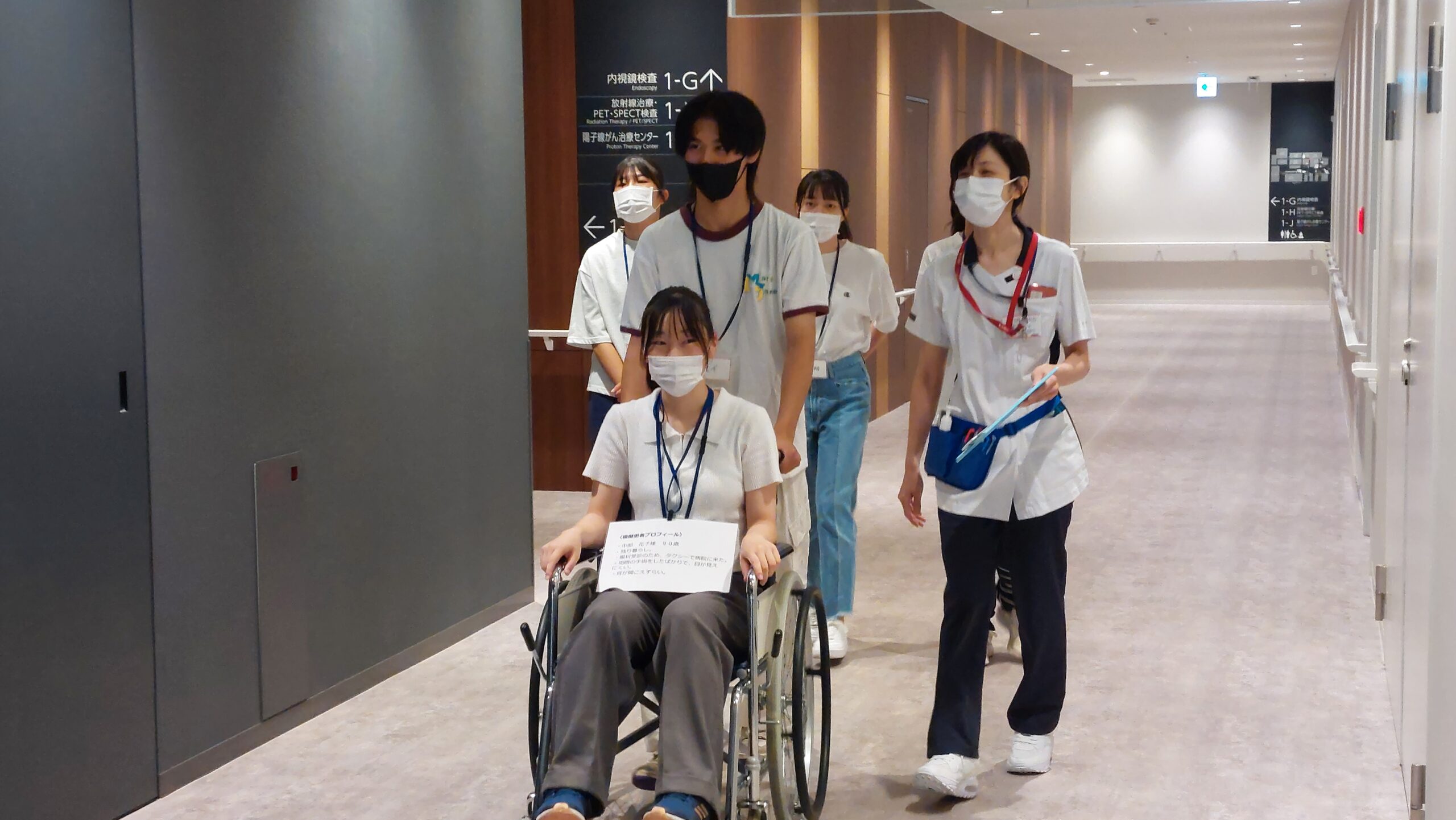 男子高校生が車椅子を押し、患者役の高校生とともに廊下を移動している様子