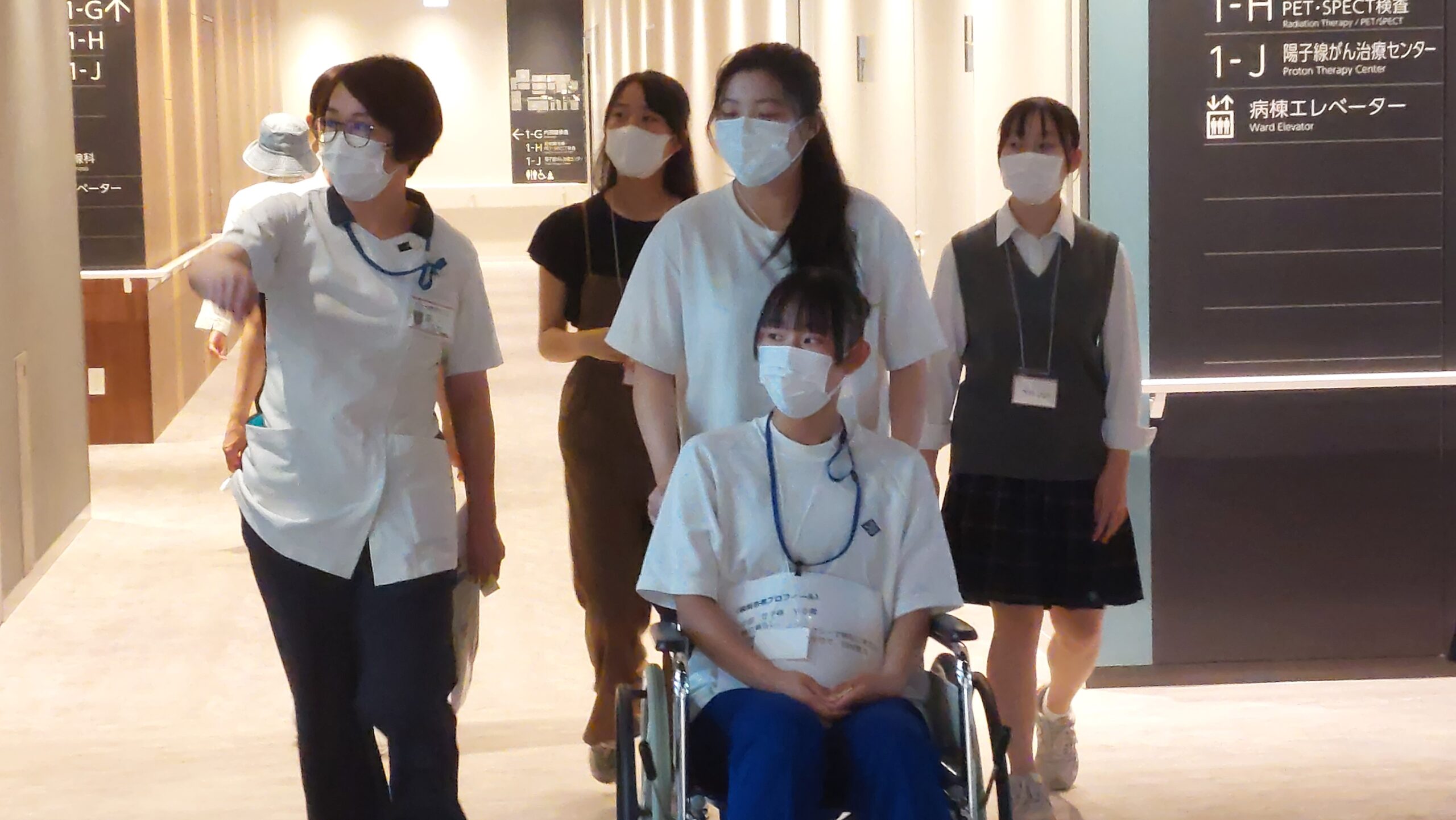 高校生が車椅子に乗り、看護師と参加者とともに院内を移動している様子