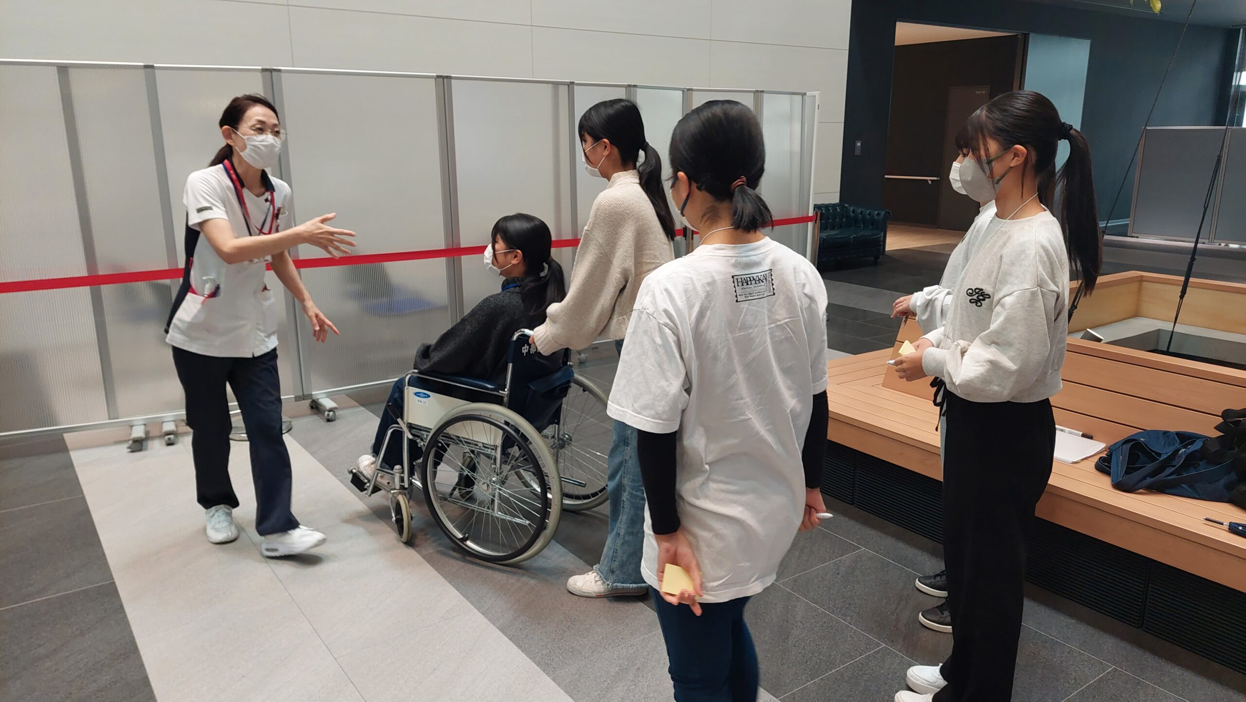高校生が車椅子を押しながら看護師の説明を聞いている様子