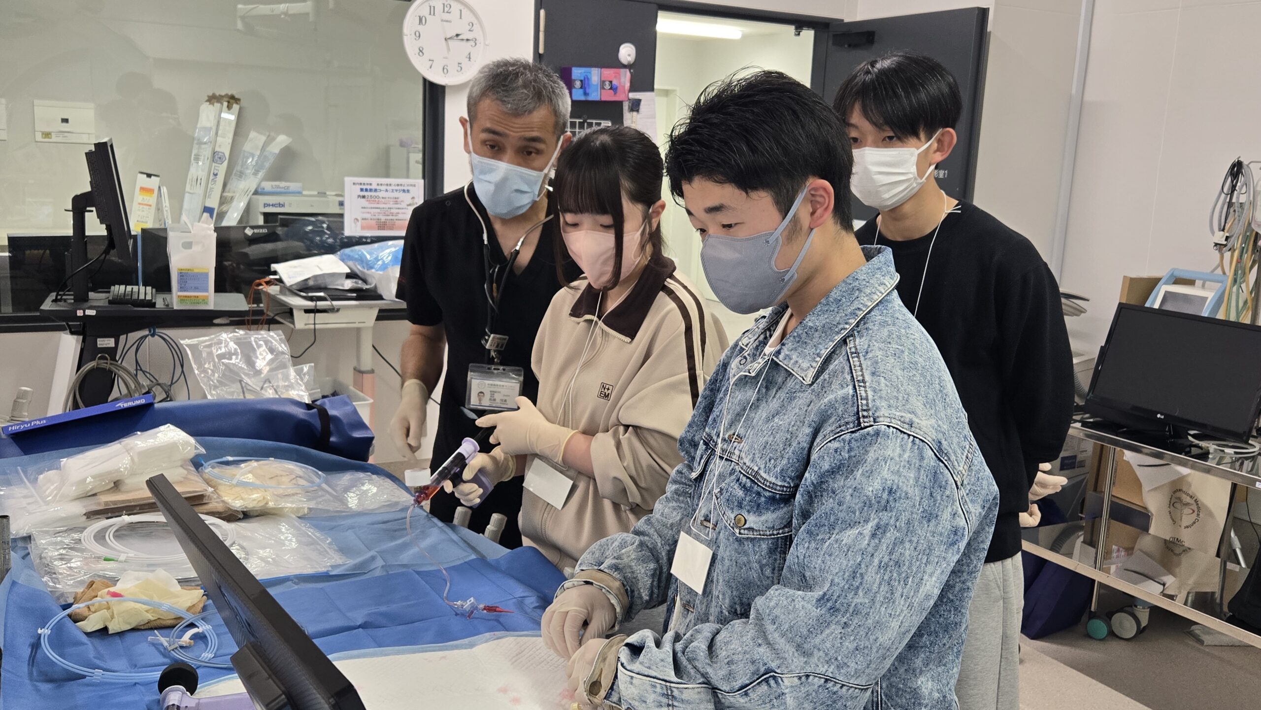 医療従事者の指導を受けながらカテーテル治療の機器に触れる高校生