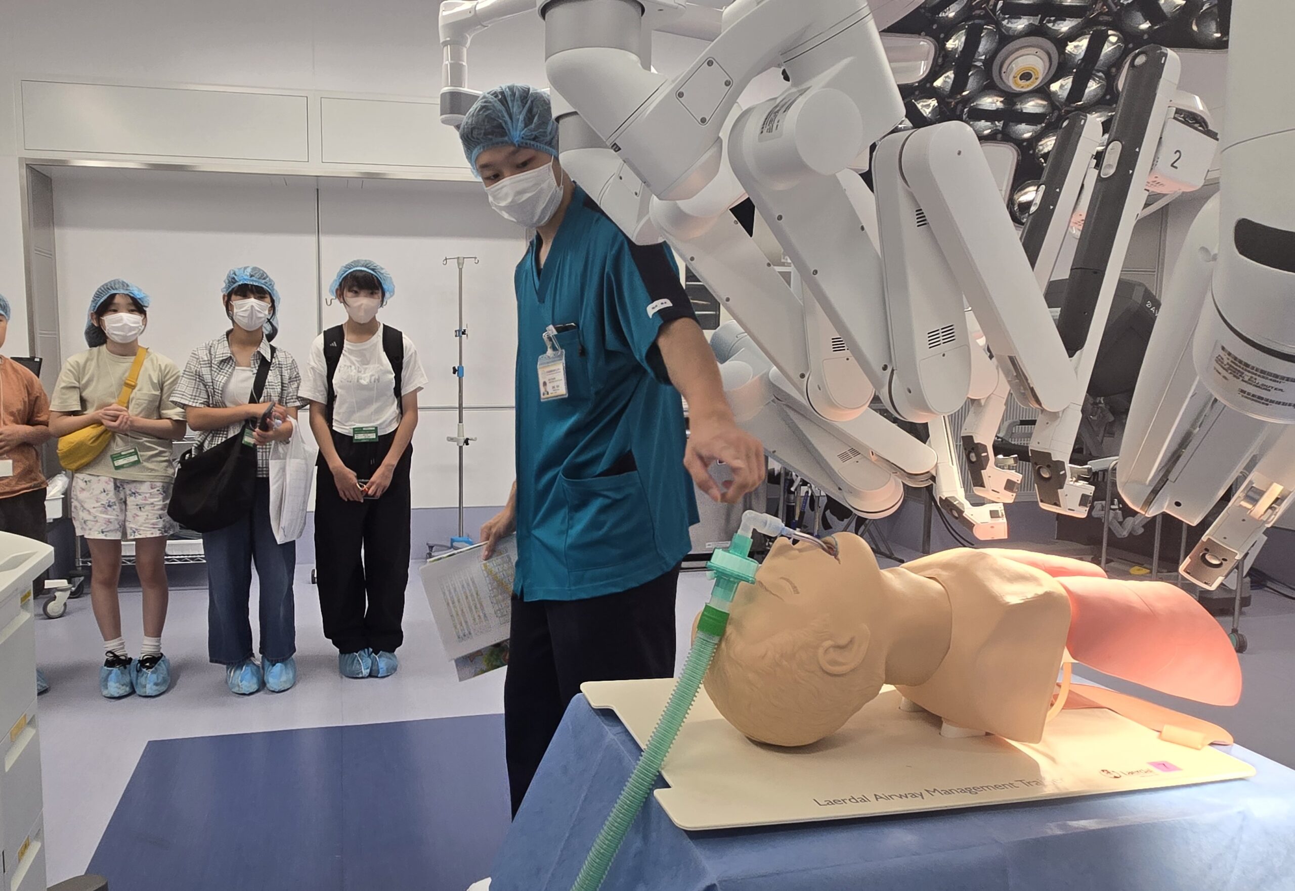 手術室で手術支援ロボットについて説明を受ける小中学生