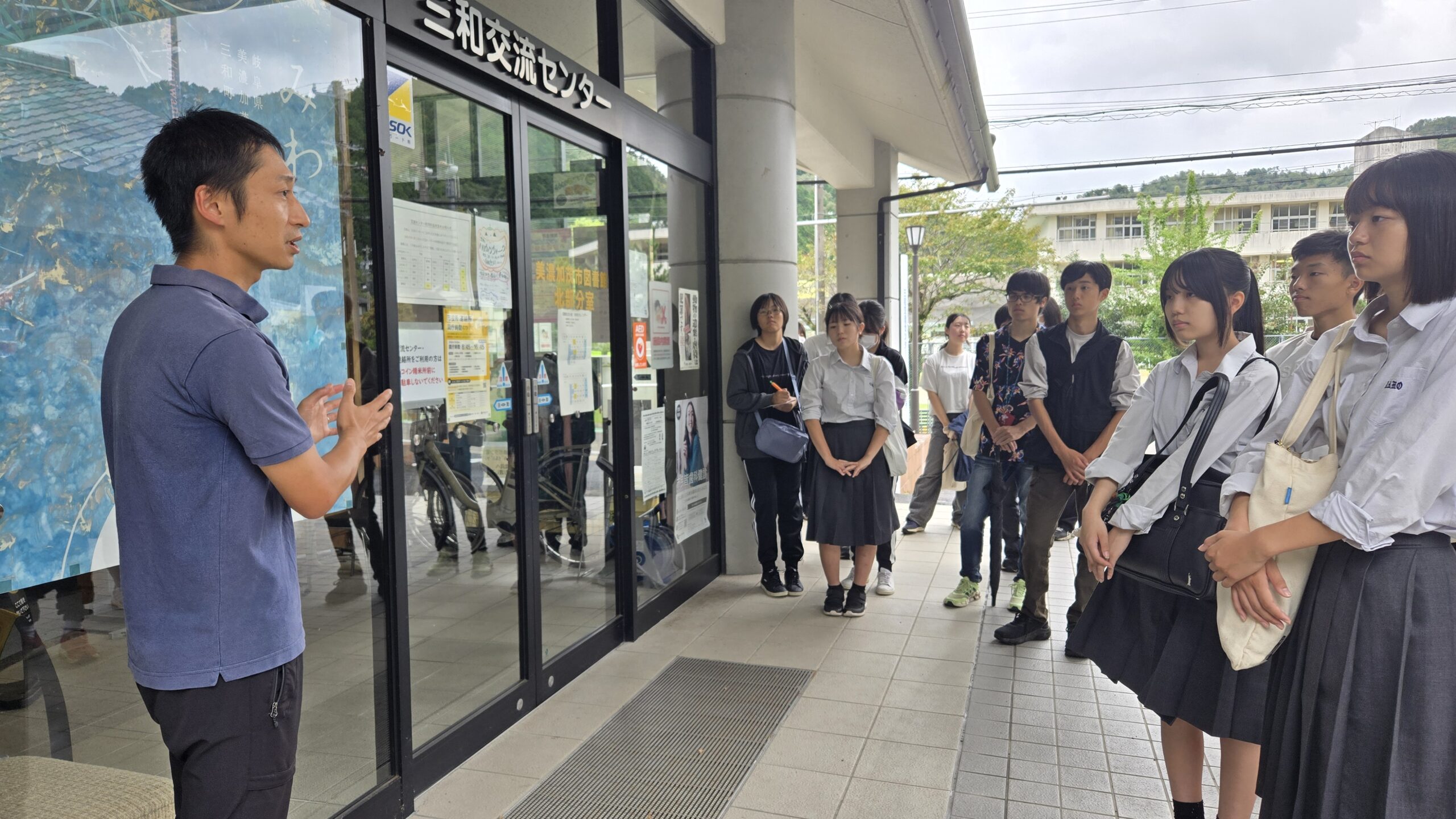 三和交流センター前で美濃加茂市職員の天池さんから地域について話を聞く高校生たち