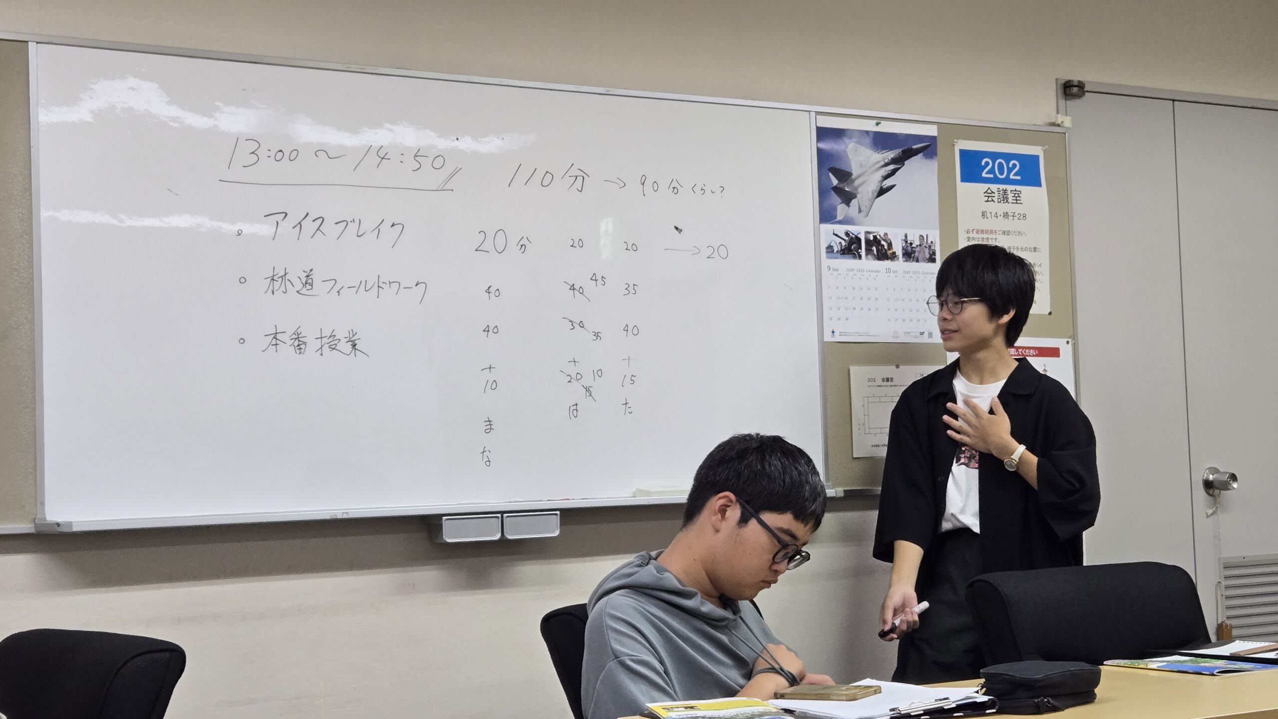 ホワイトボードを使って本番授業の時間割を説明する高校生