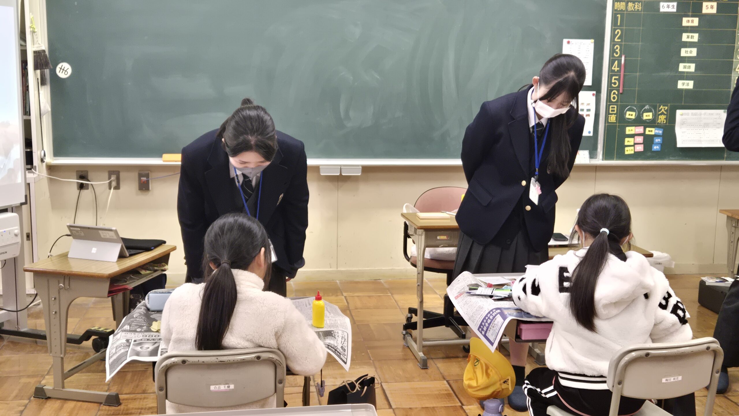 高校生と小学生が床に広げた模造紙へ絵や自然物を加える様子