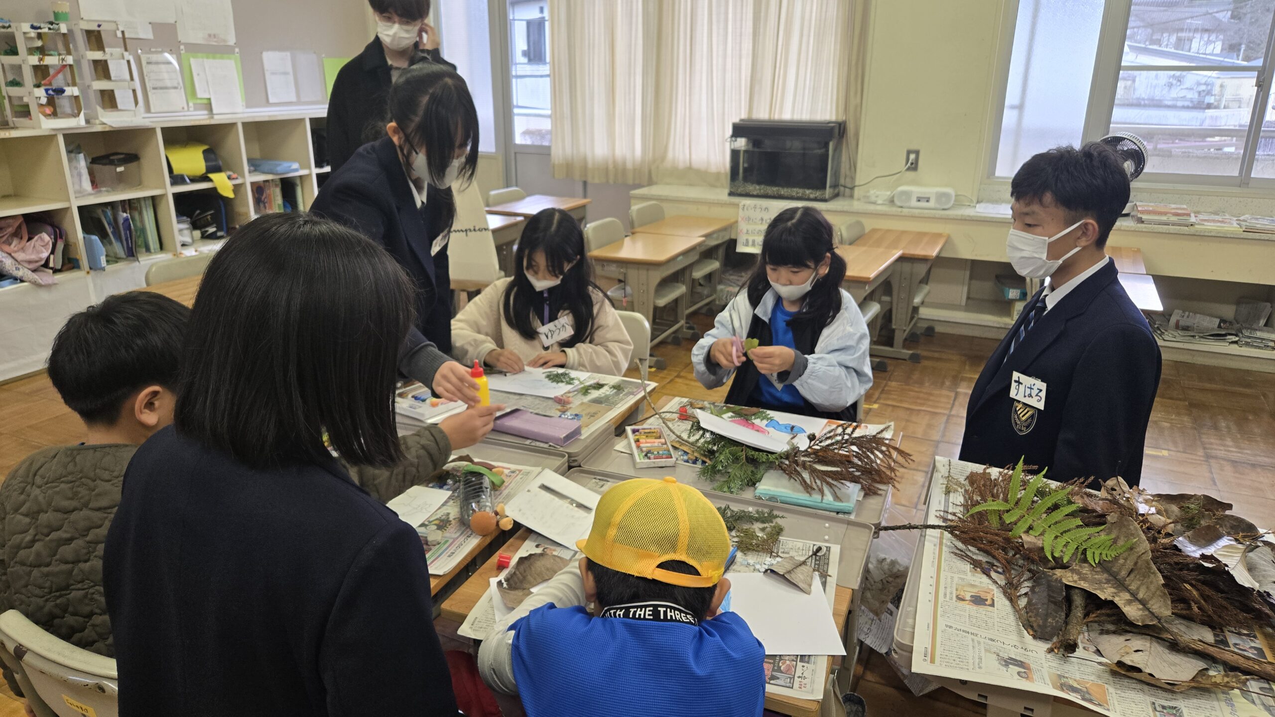 机の上に葉や枝を広げ高校生と小学生が制作する様子