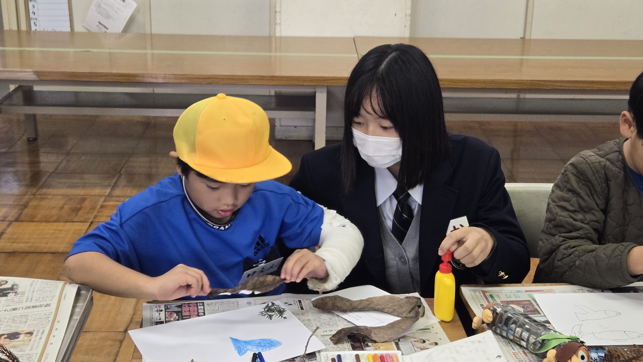 高校生が小学生の自然素材を使った制作を手伝う様子